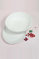 Deep white porcelain shell bowl resting on the oval shell dish, with fine ridges fanning out like a seashell