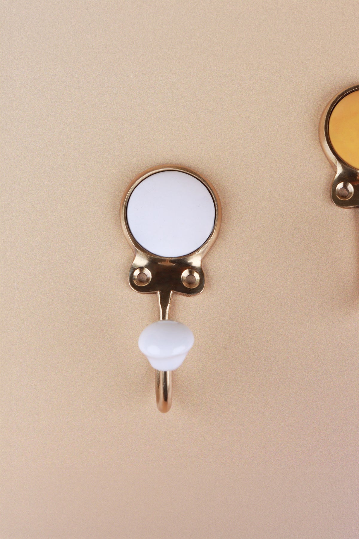 White ceramic coat hook: white disc in a gold-tone frame with a white ceramic knob