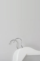 Close-up of two white wooden coat hangers showing the metal hooks