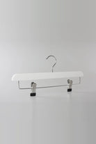 White wooden clip hanger with a metal hook and two clips, seen from an angle